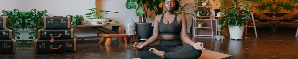 Person sitting cross legged and meditating in a room with plants