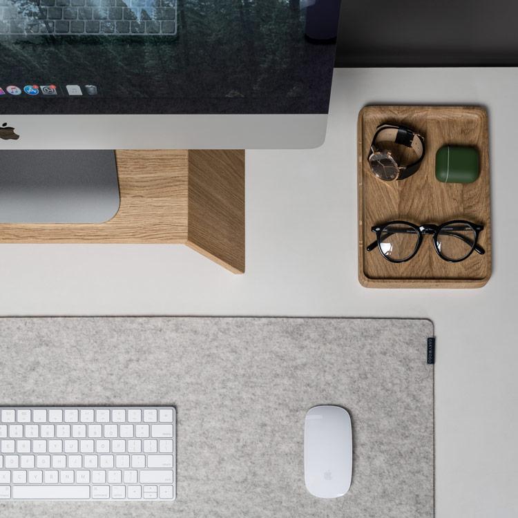 Photo of a workspace with a desktop, keyboard and mouse, and a basket with glasses, watch and an air pods case