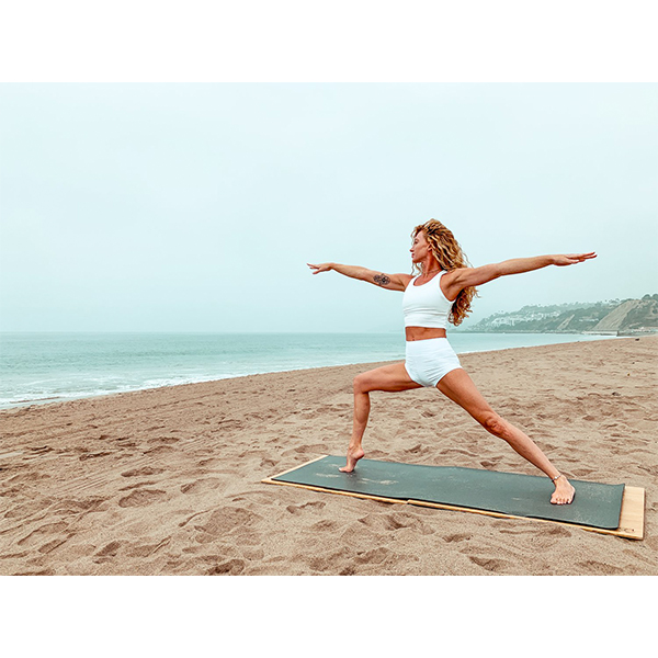 A person doing a Warrior I yoga pose on a yoga mat at the beach and using The Root Board from EarthHero
