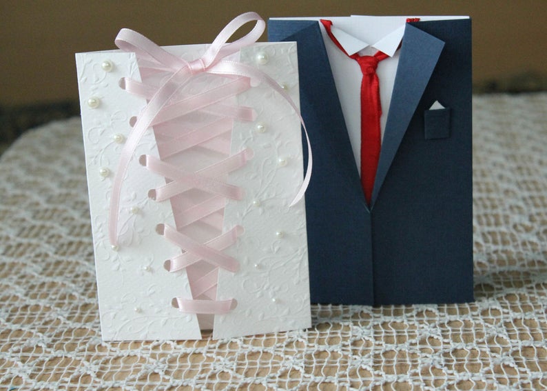 A photo of handmade bachelor party cards, one that is designed like the back of a wedding dress and the other like a groomsman's suit.